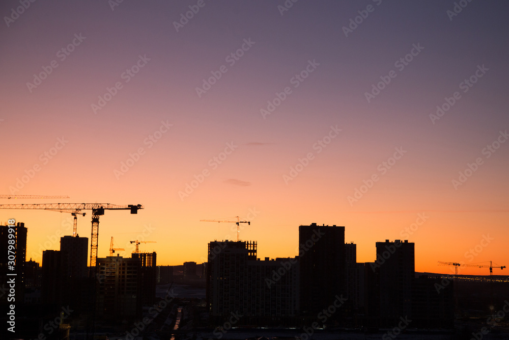 Cranes and construction of modern high-rises. Silhouette of houses under construction at sunset.