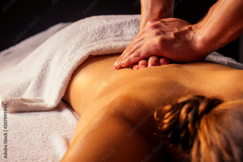 Fototapeta premium young indian woman lying on the table and getting ayurvedic massage with organic oil or honeyed in dark room.massagist male pouring out client back