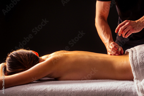 Masseur hands doing back massage to client in spa center in dark room