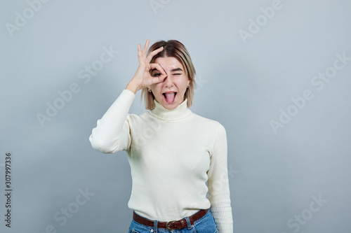 Young beautiful caucasian woman showing ok sign gesture near eyes wearing white shirt on isolated gray background