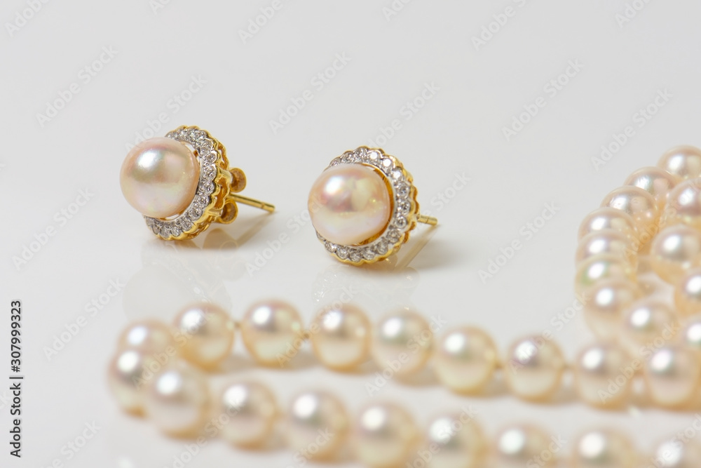 Pair of natural pearl earrings on white with pearl necklace in the background. Pair of natural pearl earrings on white with pearl necklace in the background.