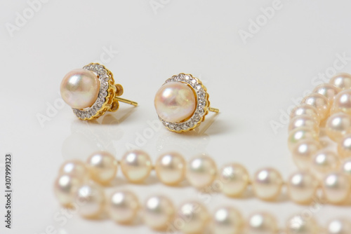 Pair of natural pearl earrings on white with pearl necklace in the background.