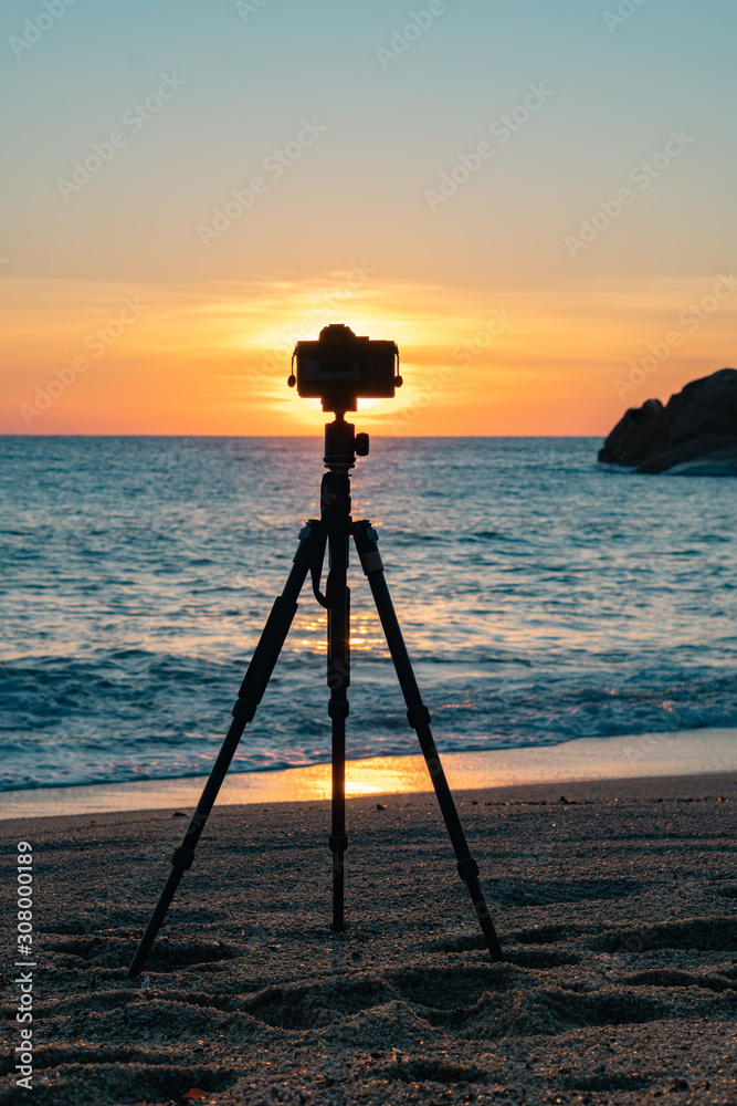Camera standing on a tripod on the beach against the background of dawn Camera standing on a tripod on the beach against the background of dawn