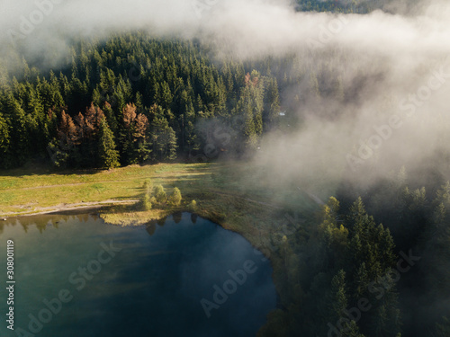 Coniferous forest surrounded by blue lake in the mist. Aerial view of Saint Anna Lake in Romania,Transylvania.