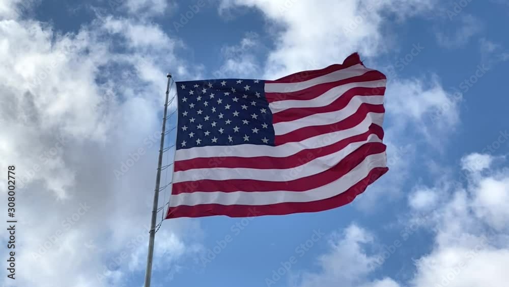 United States flag flying in breeze, blue sky and cloudy background, slow motion