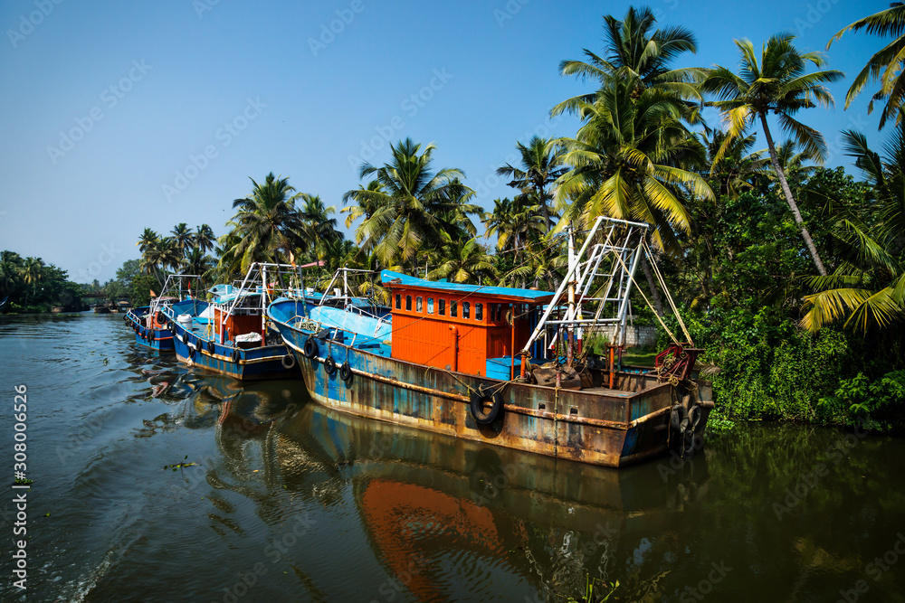 Ocean fishing boats along the canal Kerala backwaters shore with palm trees between Alappuzha and Kollam, India