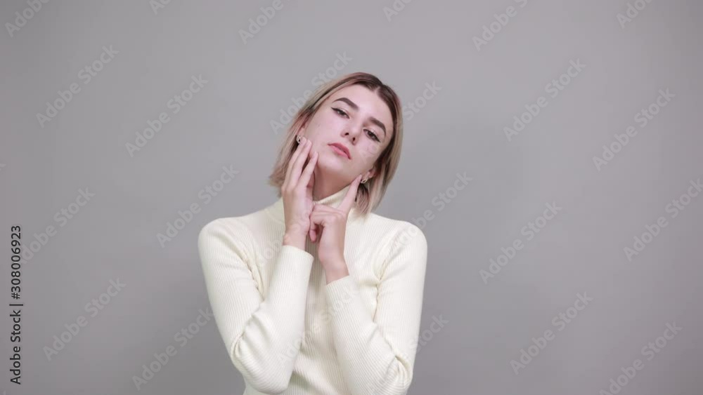 Young beautiful caucasian woman keeping hand on face, model gesture wearing white sweater on isolated white background Young beautiful caucasian woman keeping hand on face, model gesture wearing white sweater on isolated white background