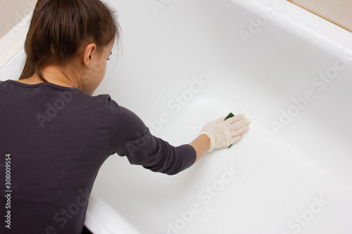 A girl in gloves washes a white bath with a foam sponge