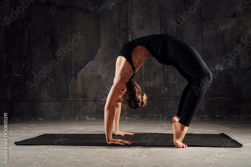 Young fitness woman making gymnastic bridge or yoga on the mat, doing exercises. Studio shot on black background.