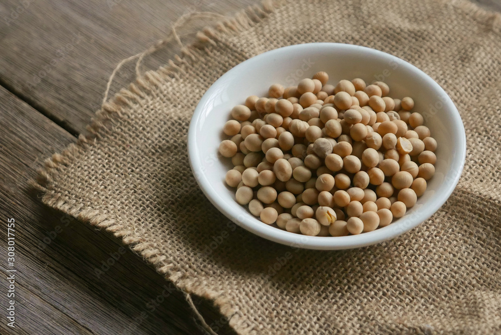 Soybeans in a white plate on rug sack on wooden background. Soybeans in a white plate on rug sack on wooden background.