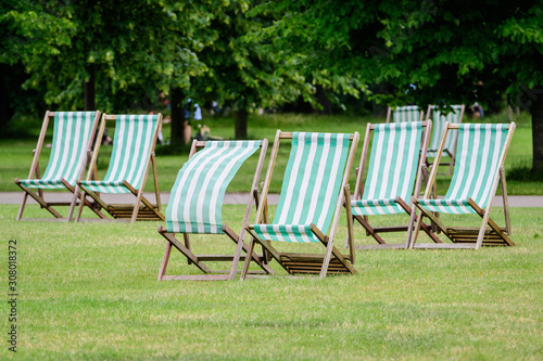 Six white and green striped outdoor garden chairs displayed in fresh green grass in a park in London, Great Britain, during a sunny summer day, natural green background in a big city © Cristina Ionescu