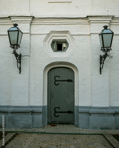 Old-style closed wooden doors in a stone wall which are adorned by hand hammered iron accents and door lanterns. Close-up.