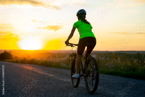 Beautiful girl cyclist rides a bicycle on the road in the sunset. Healthy lifestyle and sport. Leisure and hobbies