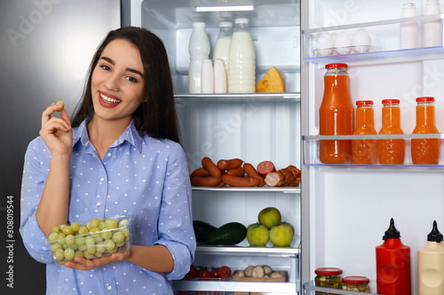 Happy young woman with grape near open refrigerator
