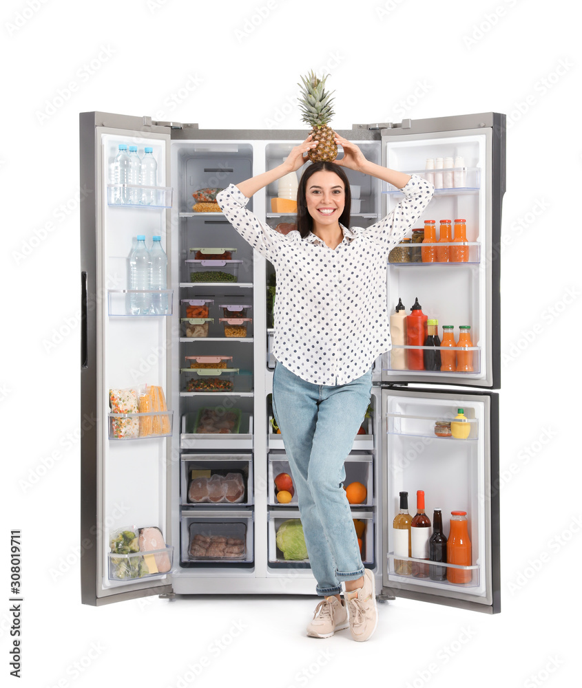 Young woman with pineapple on head near open refrigerator against white background Young woman with pineapple on head near open refrigerator against white background