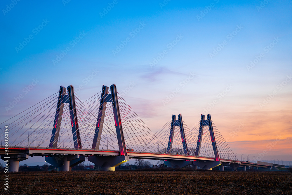 Obraz premium Monumental, lighted, new modern double cable-stayed bridge over Vistula River in Krakow, Poland during sunset.