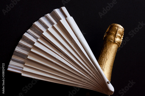 FAN NEXT TO BOTTLE OF CHAMPAGNE ON BLACK BACKGROUND. CELEBRATION OF HOLIDAYS IN SPAIN