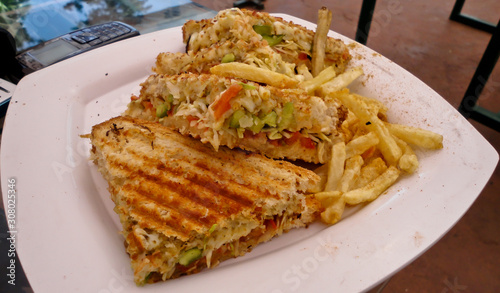 Veg grilled sandwich with french fries, sauce and chilli flakes. Morning breakfast of hot grilled sandwich contains smashed potatoes and vegetables