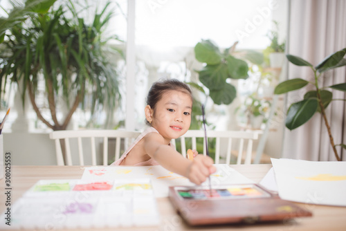 Cute little Asian Girl enjoying Painting at home with paper, water colour and art brush.
