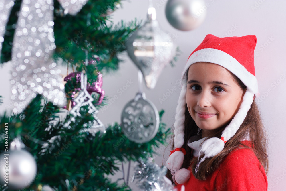 Portrait of girl dressed as Santa Claus next to Christmas tree. Portrait of girl dressed as Santa Claus next to Christmas tree.