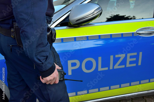 A policeman beside a german police car with a mobile radio in his hand.