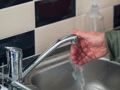 A close-up of a man washing his hand under a stainless steel mixer tap with running water in the kitchen