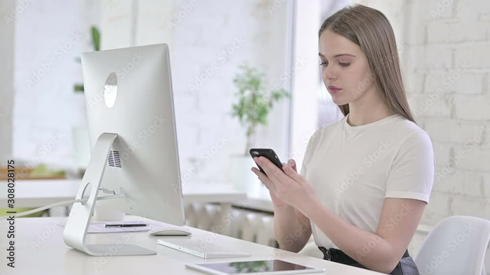 Attractive Young Woman using Smartphone and working on Desktop Attractive Young Woman using Smartphone and working on Desktop