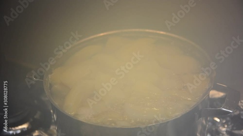 pieces of potatoes are boiled in a pan on a gas stove.