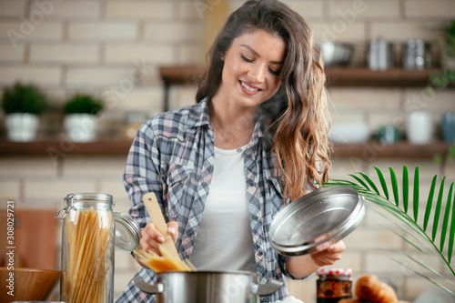 Young woman in kitchen. Beautiful woman making pasta. Cooking delicious dinner. © JustLife