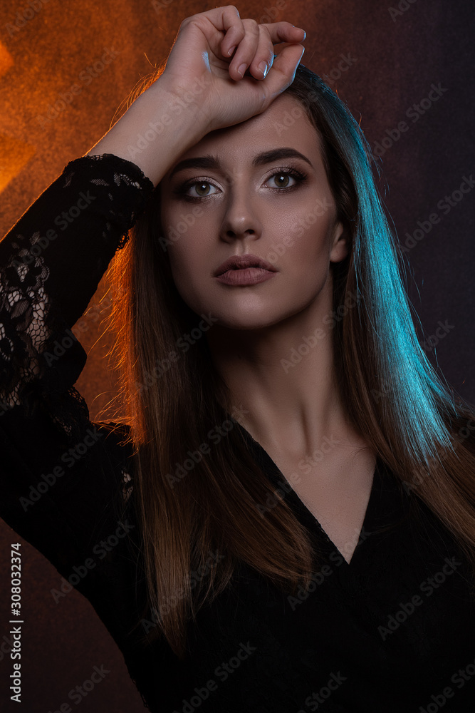 Obraz premium Close up beauty portrait of young beautiful woman in color backlight dressed in black. Studio shot.
