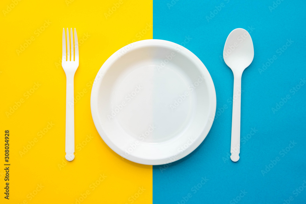 Plastic white fork, spoon and plate on yellow and blue background. Cooking utensil. Top view. Minimalist Style. Copy, empty space for text Plastic white fork, spoon and plate on yellow and blue background. Cooking utensil. Top view. Minimalist Style. Copy, empty space for text