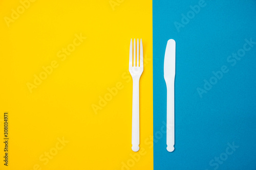 Plastic white fork and knife on yellow and blue background. Cooking utensil. Top view. Minimalist Style. Copy  empty space for text