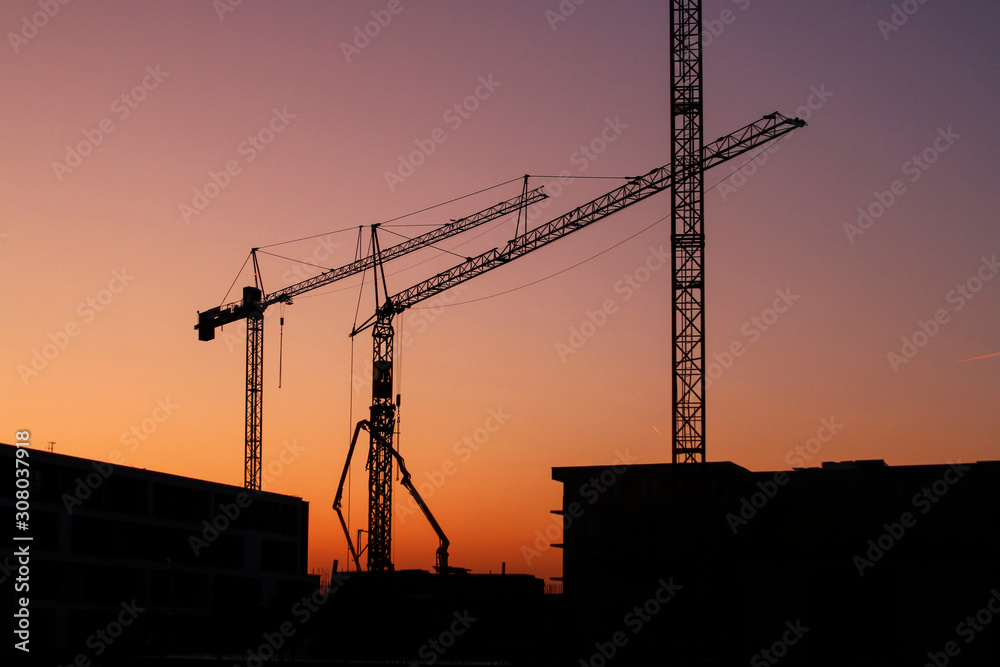 Construction cranes seen against the backdrop of the setting sun.
