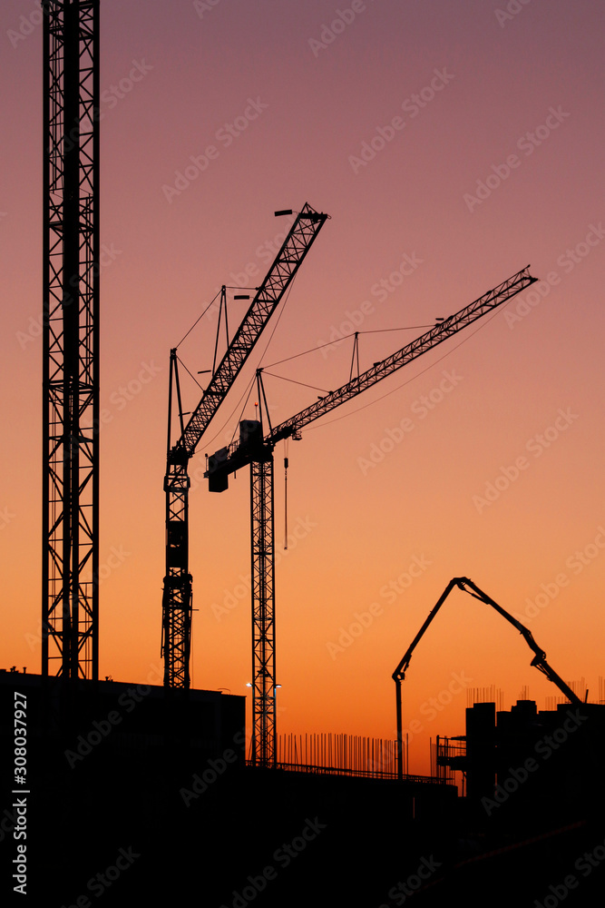 Construction cranes seen against the backdrop of the setting sun.