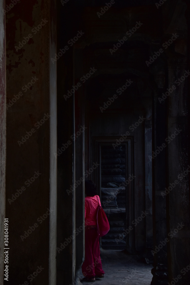 A woman dressed in red, walking in a dark temple corridor.