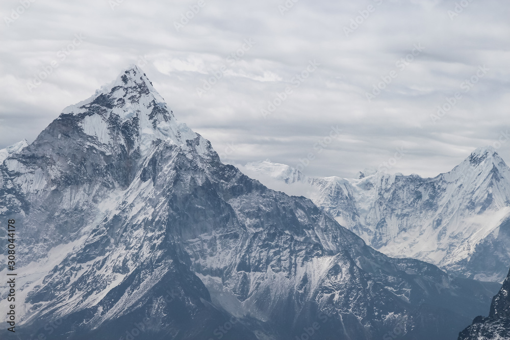 Close up view of Ama Dablam mountain peak in cloudy day near Cho La pass in Sagarmatha national park in Himalayas. Snow lumps at the very top of the mountain. Copy space.
