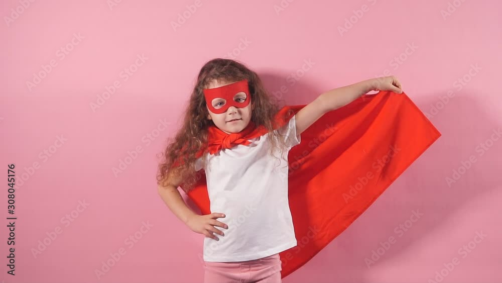 Attractive cute kid wearing red superhero suit and mask standing at isolated over pink background. Attractive cute kid wearing red superhero suit and mask standing at isolated over pink background.
