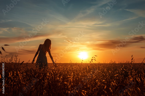 Young woman standing on a wheat field with sunrise on the background