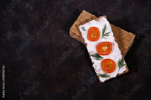 Photos crispbread with curd cheese and cherry tomato on a dark background