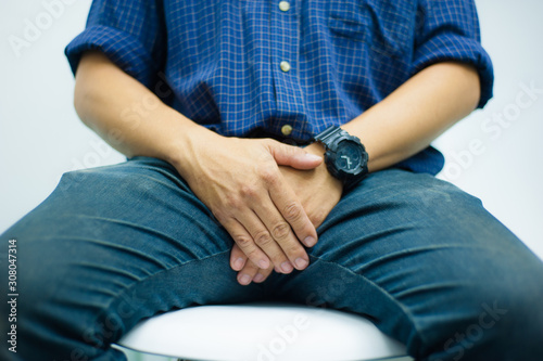 Concepts about male health problems. Close-up of a man sitting on a chair and using his hands to close the groin.