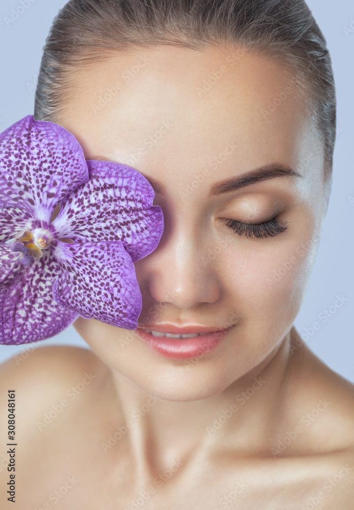 Portrait of a beautiful happy woman with clean skin and with nude make-up. She holds a beautiful purple orchid near her face.Cosmetology skin care and make-up. Portrait of a beautiful happy woman with clean skin and with nude make-up. She holds a beautiful purple orchid near her face.Cosmetology skin care and make-up.