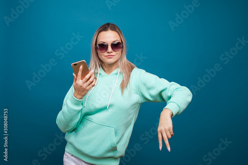 Stylish trendy hipster girl in the blue hoodie with the hood uses a smartphone.