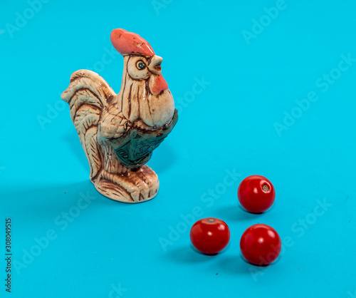 Clay figure of a rooster and cherry tomatoes on a turquoise background.