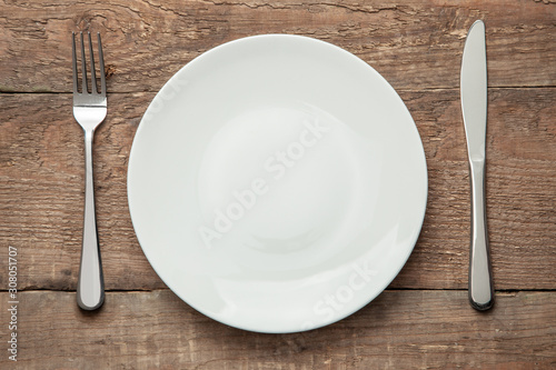 Fototapeta Empty white plate with knife and fork on a wooden table
