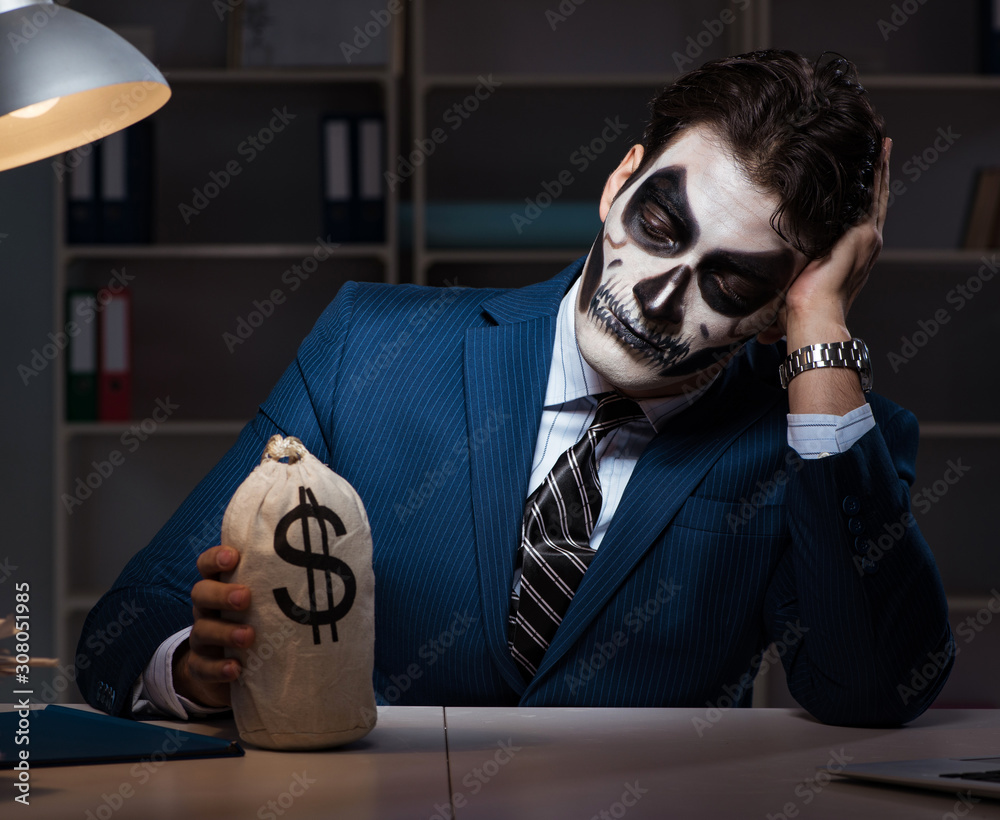 Businessman with scary face mask working late in office Businessman with scary face mask working late in office