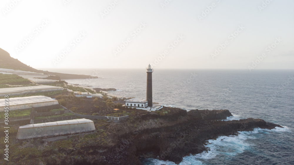 Lighthouse in a rocky cliff and banana tree around on the atlantic ocean. Coastline in the sunset. Light orientation to navigate and guidance in the sea for the marine.