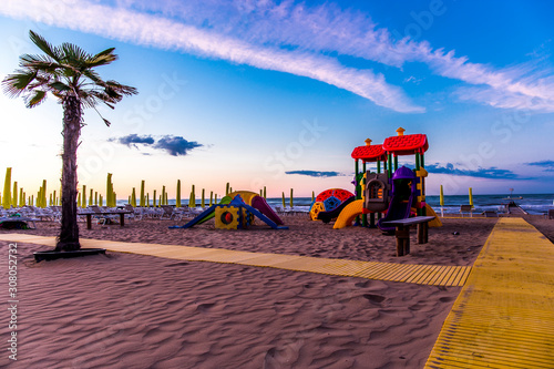 Playground for children on the beach with pavement and a palm at sunrise. Jesolo, Italy.