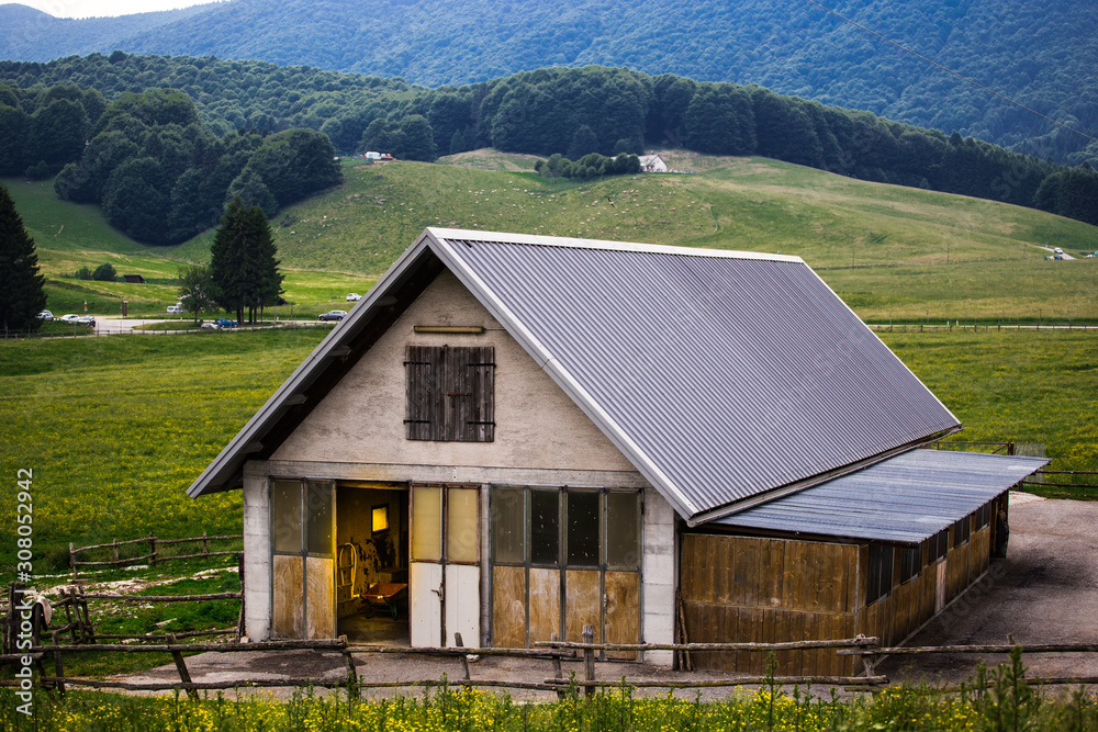 Rural building with stables inside with meadow, forests and hills in the background.