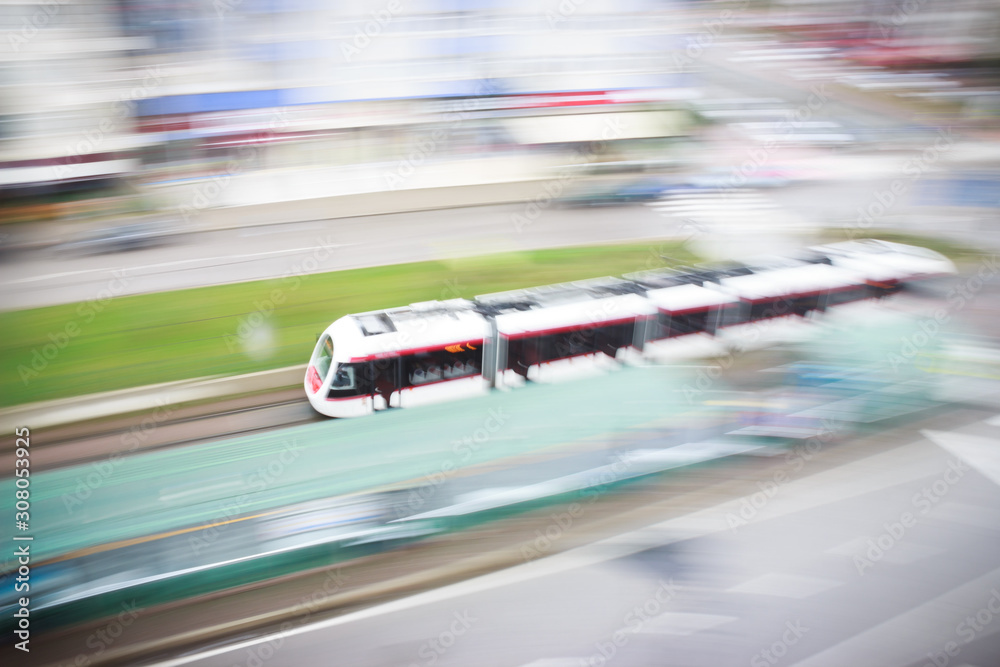 Fast moving blurred tram approaching to train station in city landscape. Light rail system in city.