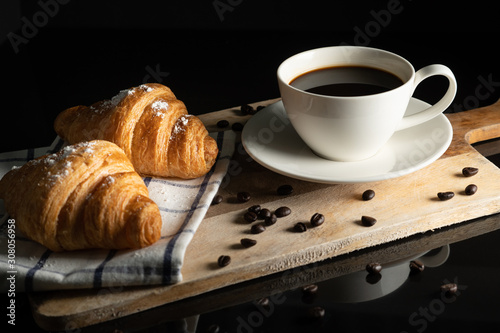black cofffee in white cup and wheat flour sprinkle croissant on towel on board wood with black background